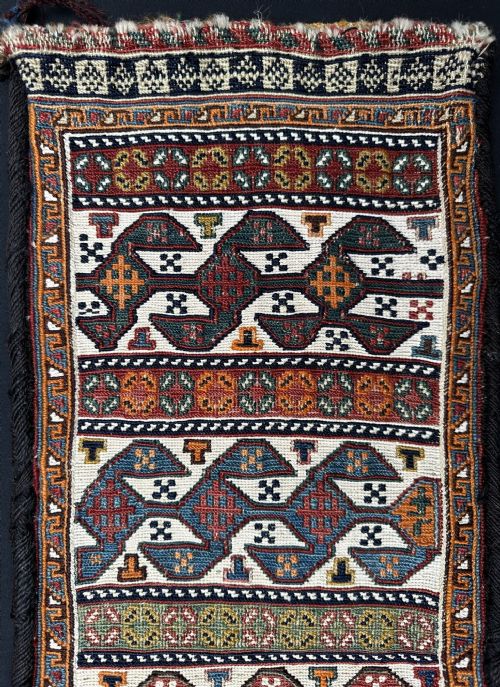 fig 1. An antique Persian Qashqai flat-woven bag featuring repeating geometric motifs in red, blue, and terracotta hues set against a cream wool ground.