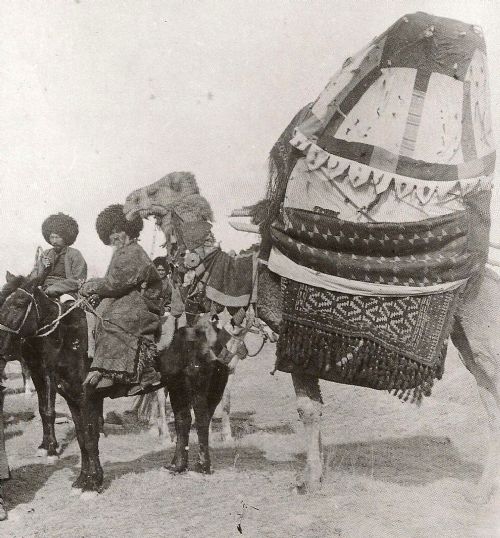fig 1. A pentagonal hand-knotted Turkmen wool asmalyk featuring geometric diamond lattice motifs in red, ivory, and navy blue with a long multi-coloured fringe along the bottom edge.