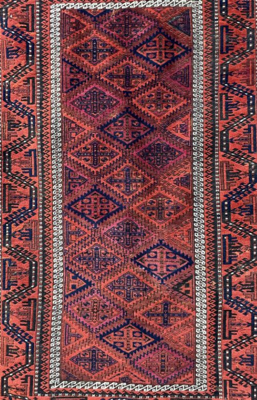 fig 1. A rectangular hand-knotted wool rug featuring repeating geometric diamond latch-hook patterns in terracotta red, deep blue, and ivory accents.