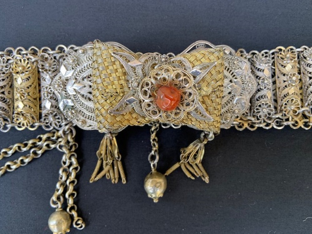 An antique silver and gilt filigree waist belt featuring a central woven bow buckle set with a red carnelian cabochon and dangling chain tassels.
