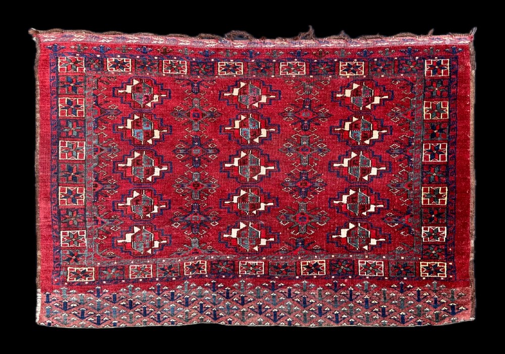 A rectangular handwoven antique Turkmen Chuval wool textile featuring geometric red and navy motifs with decorative borders.
