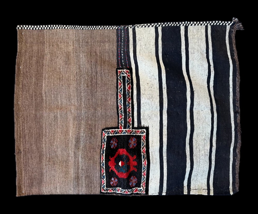 An antique hand-woven Persian wheat sack featuring plain natural brown wool on the left, vertical black and white stripes on the right, and a small pile-knotted central motif in red, blue, and black.