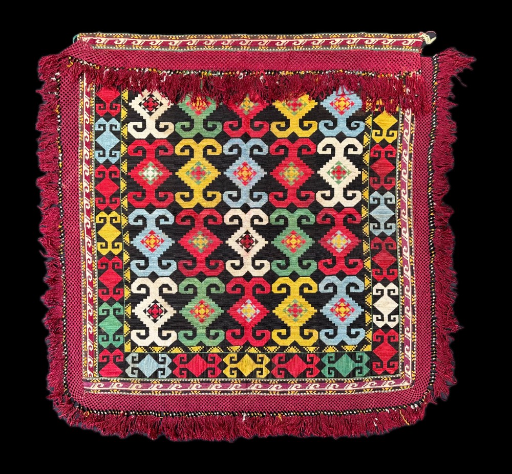A square Uzbek Lakai tribal textile bag front featuring geometric multicolored hook patterns surrounded by a fringed deep red border.