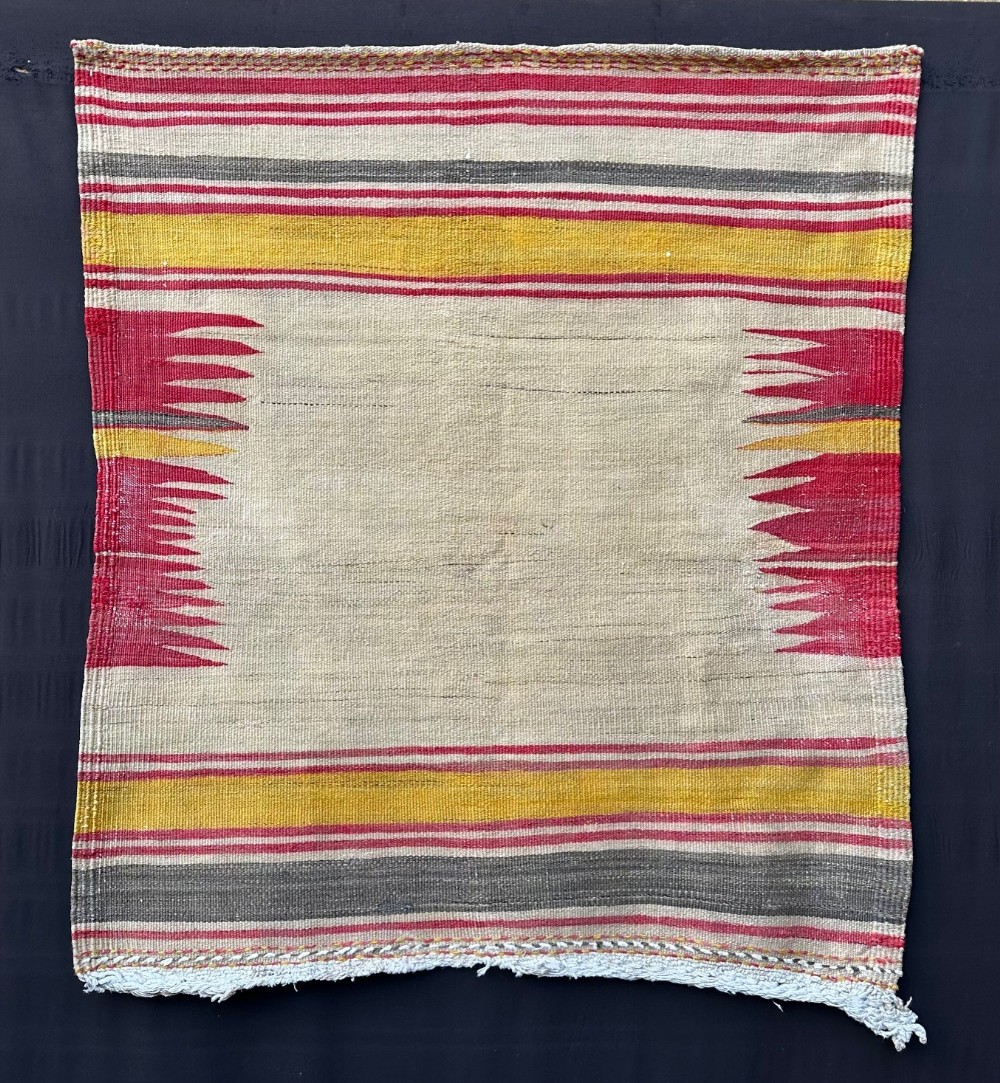 A square antique flatwoven Persian Sofreh textile featuring red, yellow, and grey horizontal stripes bordering an unpatterned central cream field with serrated side accents.