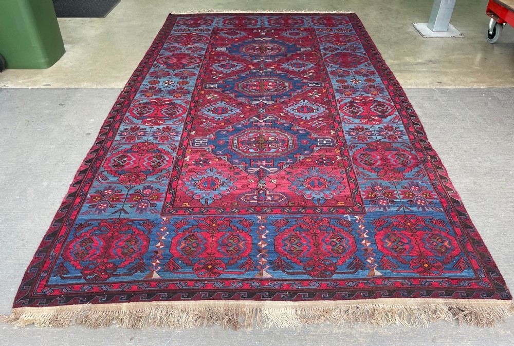 An antique Caucasian Soumak wool carpet featuring geometric Lesghi star medallions in crimson red and indigo blue.