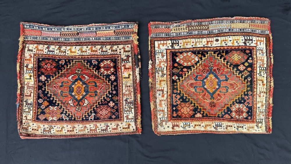 A pair of square hand-woven wool Qashqai saddlebag faces featuring central geometric diamond medallions surrounded by borders of stylised animal figures in terracotta red, navy blue, and ivory.
