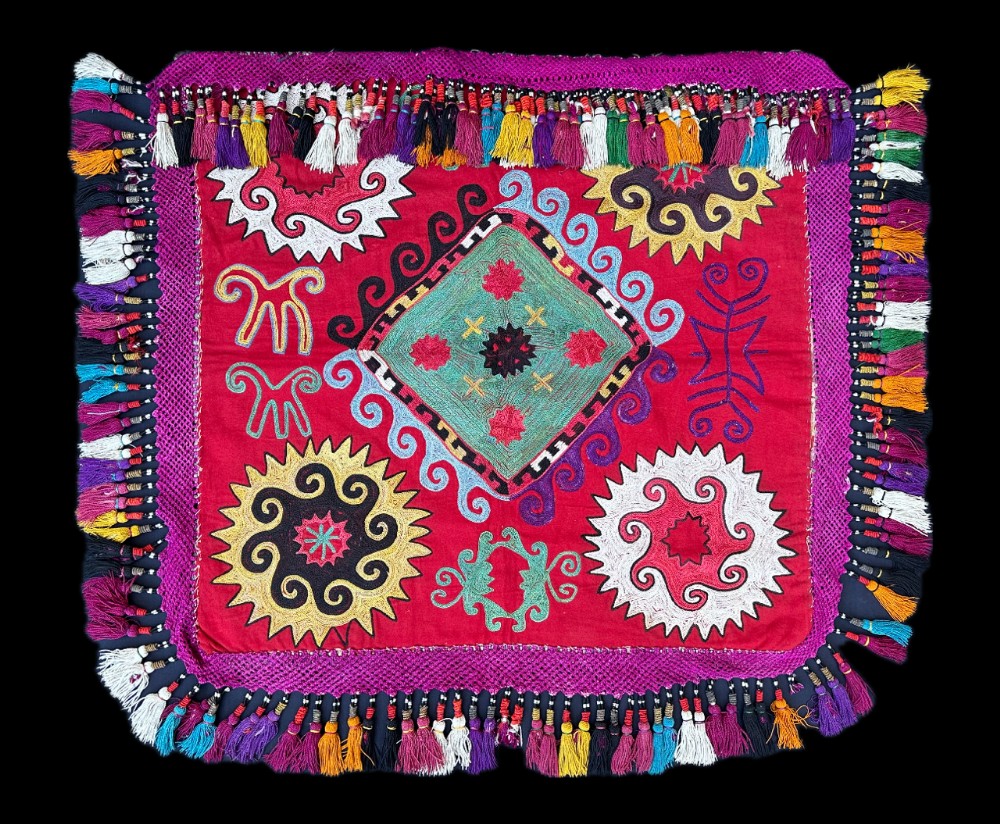 A square red silk embroidered textile featuring central diamond and sunburst motifs bordered by dense multi-coloured thread tassels.