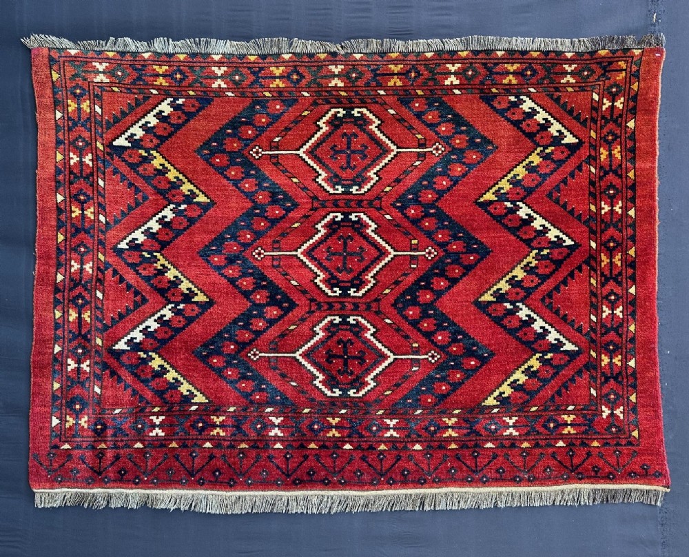 A rectangular hand-knotted wool Turkmen storage bagface featuring central diamond motifs woven in crimson red, dark navy blue, yellow, and cream with fringed edges.