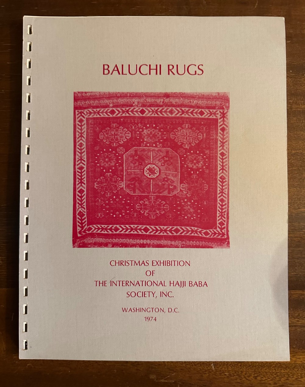 A softcover exhibition catalogue titled Baluchi Rugs featuring red text and a central red rug image against a white background.
