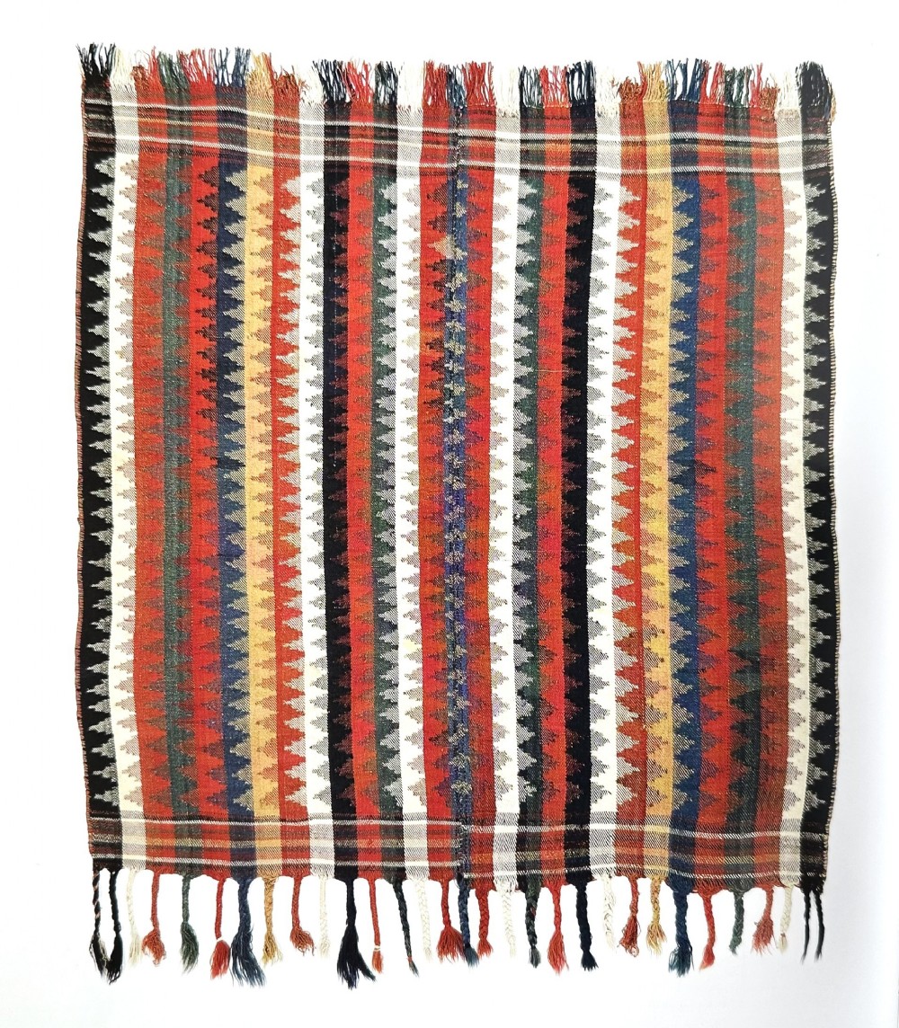An antique Persian Qashqai flatwoven wool textile featuring vertical striped bands with serrated geometric motifs in terracotta red, dark blue, yellow, and cream, complete with knotted fringe ends.