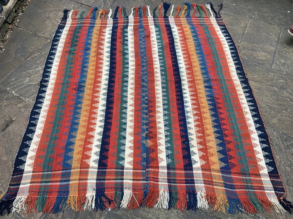 An antique Persian Qashqai flatwoven wool textile featuring vertical striped bands with serrated geometric motifs in terracotta red, dark blue, yellow, and cream, complete with knotted fringe ends. View III
