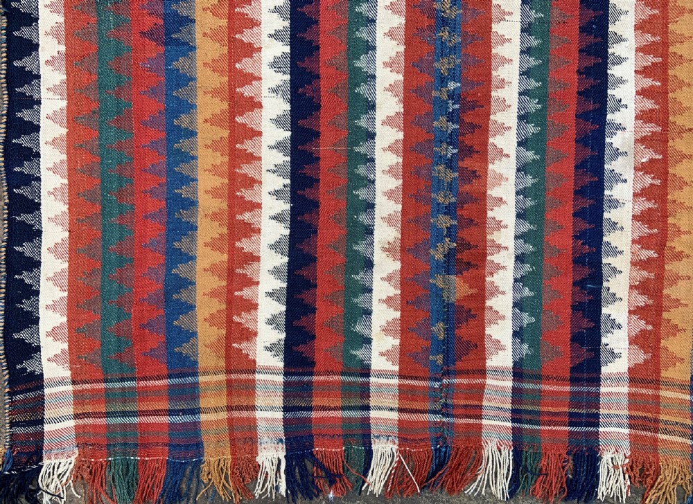 An antique Persian Qashqai flatwoven wool textile featuring vertical striped bands with serrated geometric motifs in terracotta red, dark blue, yellow, and cream, complete with knotted fringe ends. View V
