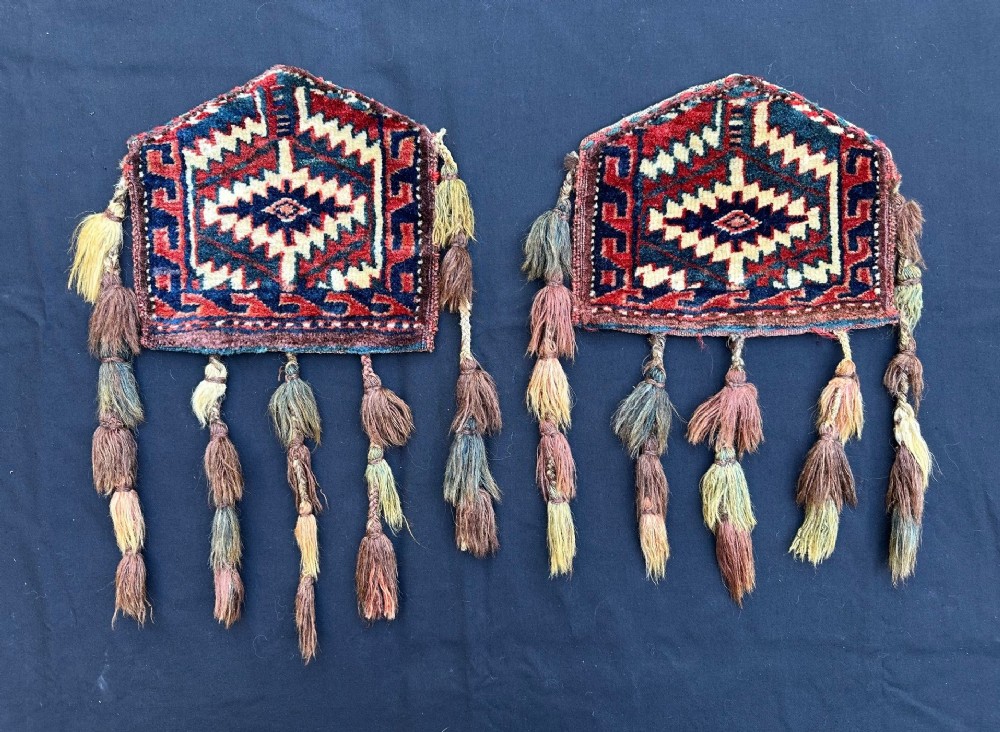 A pair of pentagonal hand-woven wool Turkmen dizlyks featuring red and blue geometric patterns with hanging wool tassels.