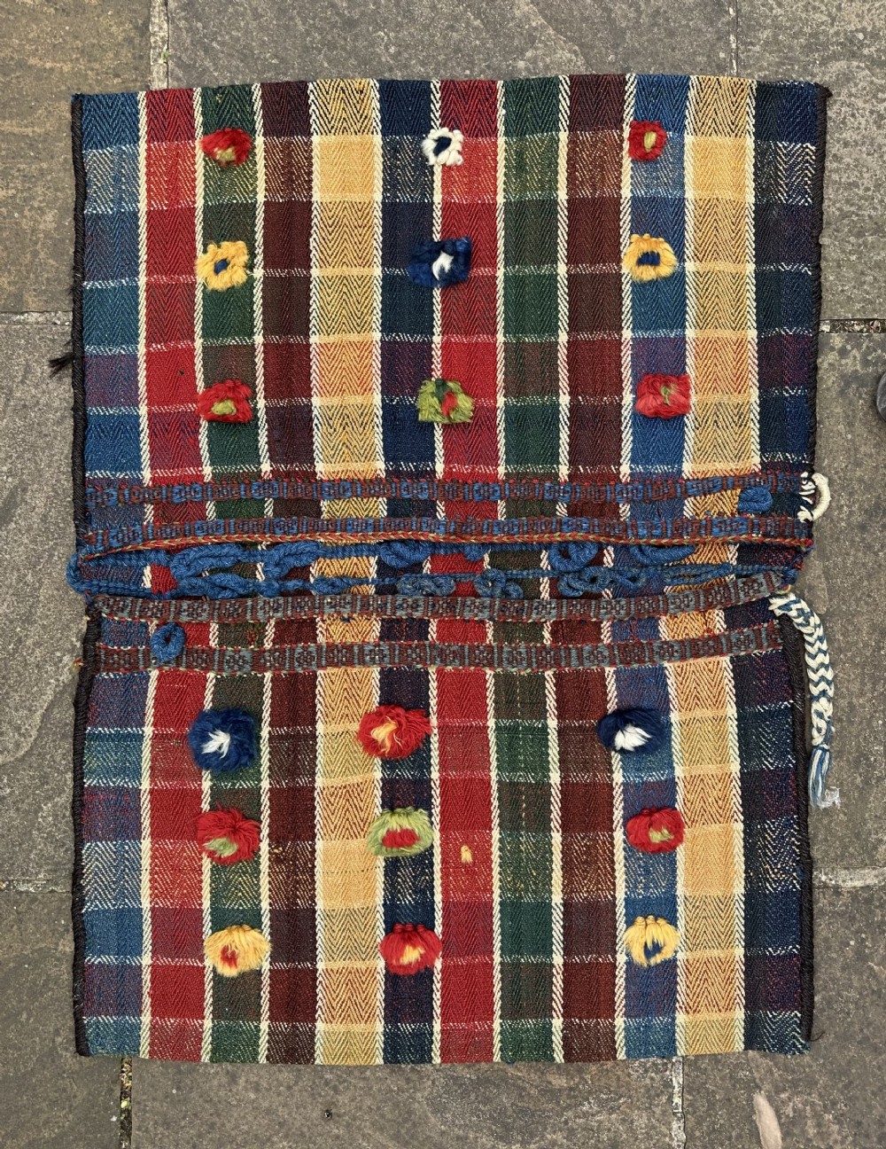 An antique handwoven wool Qashqai saddle bag featuring a colourful plaid check pattern with tufted wool embellishments and integrated closure loops.