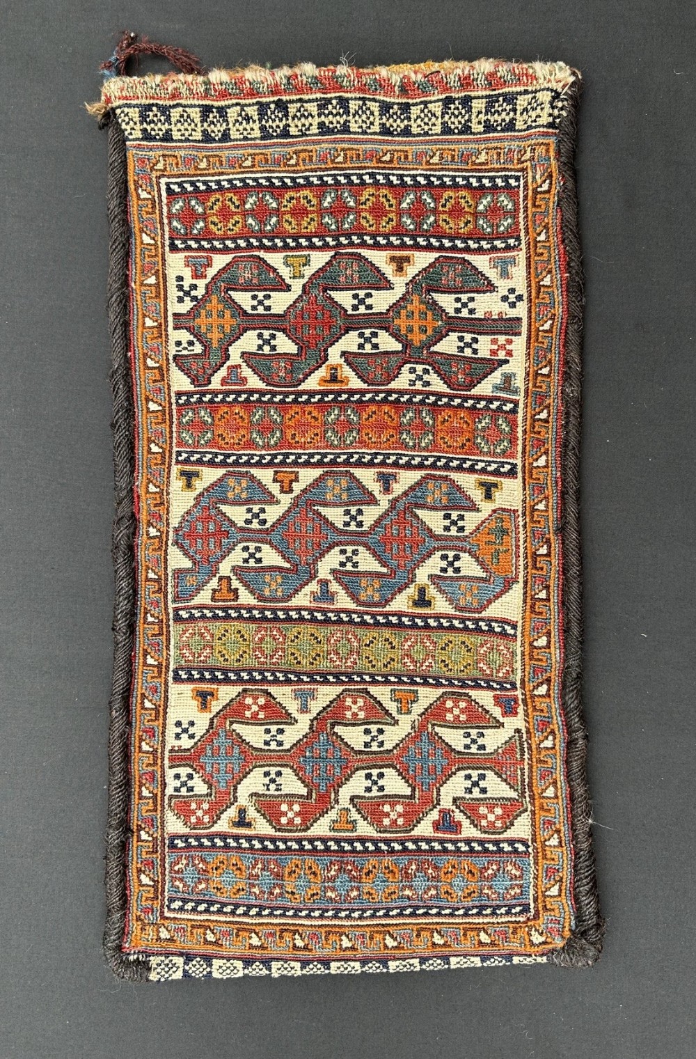 An antique Persian Qashqai flat-woven bag featuring repeating geometric motifs in red, blue, and terracotta hues set against a cream wool ground.