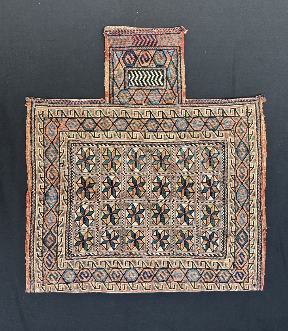 An antique Persian Afshar woven wool salt bag featuring a bottle-neck top and geometric star motifs in terracotta, blue, and ochre.