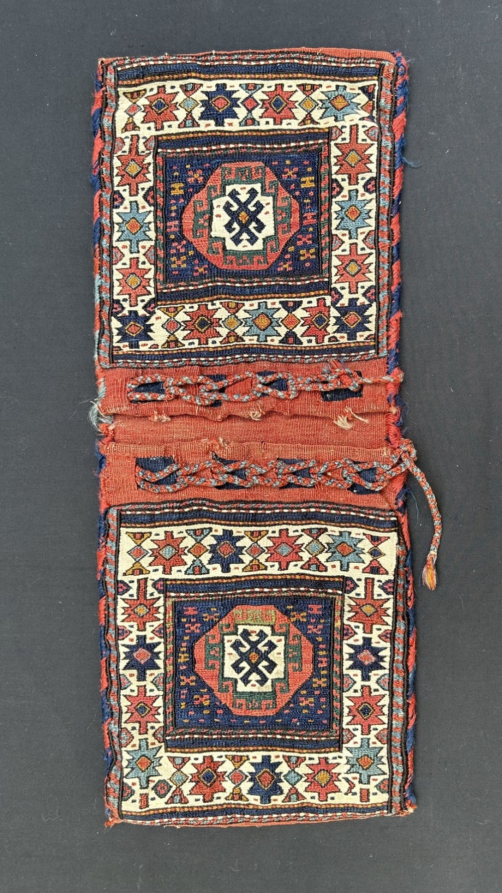 A double-pouch hand-woven wool Shahsevan saddle bag featuring geometric star motifs in terracotta red, dark blue, and ivory tones.