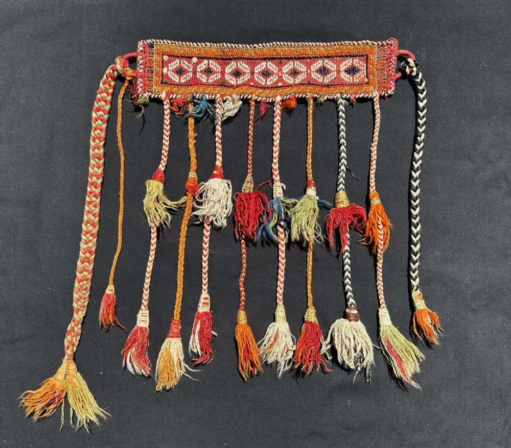 A handwoven antique Qashqai tribal horse decoration featuring a geometric band with hanging braided ropes and colourful woollen tassels.