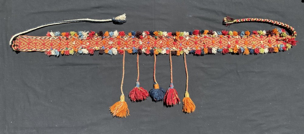 A long hand-woven antique Qashqai tribal band in red, yellow, and orange geometric patterns featuring a fringe of multi-coloured wool tassels.