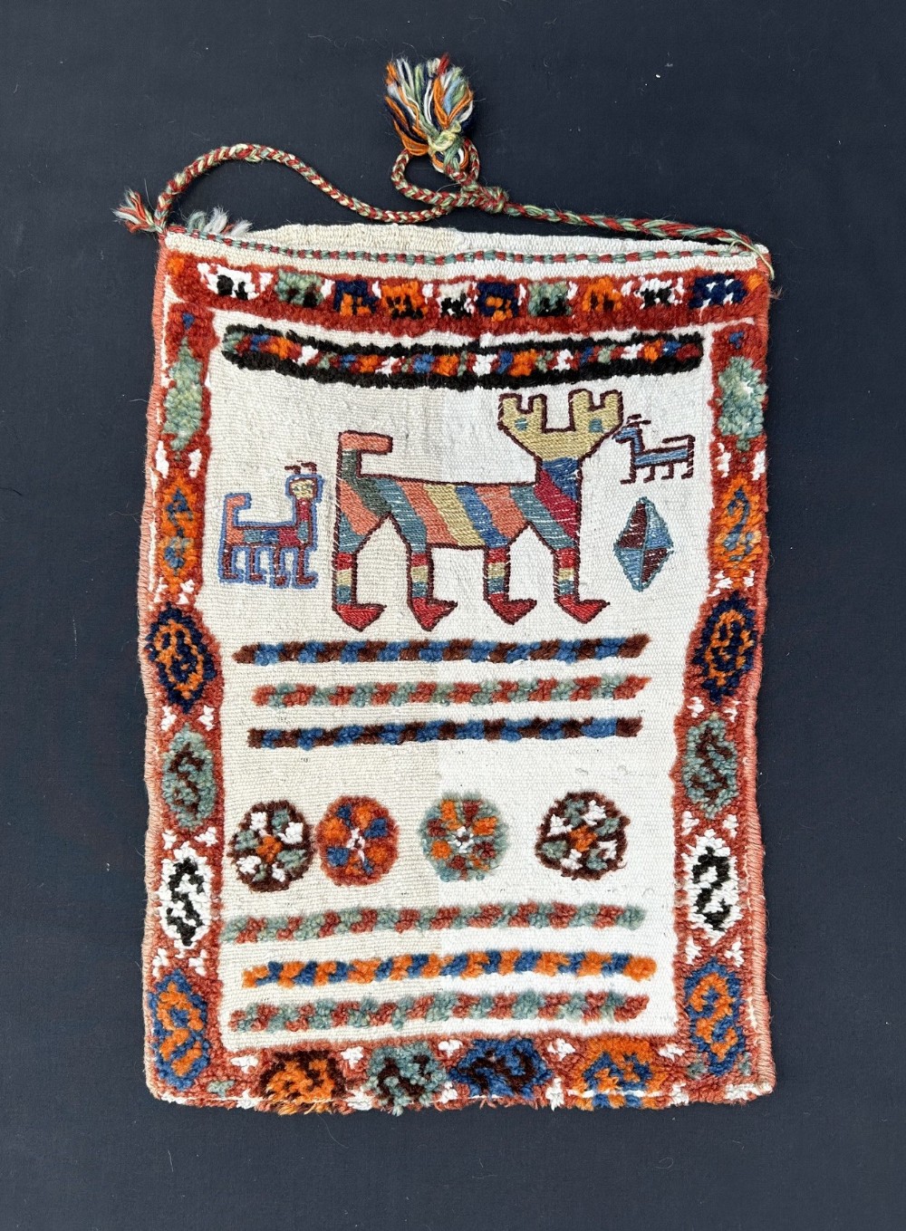 A rectangular handwoven Persian tribal bag featuring stylised animal motifs, geometric rosettes, and coloured wool pile borders against a cream background.