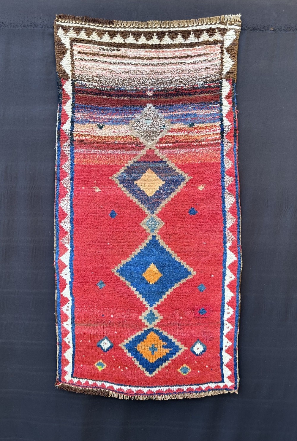An antique handwoven Persian Gabbeh rug featuring blue and yellow diamond medallions set within a red field and framed by a patterned border.