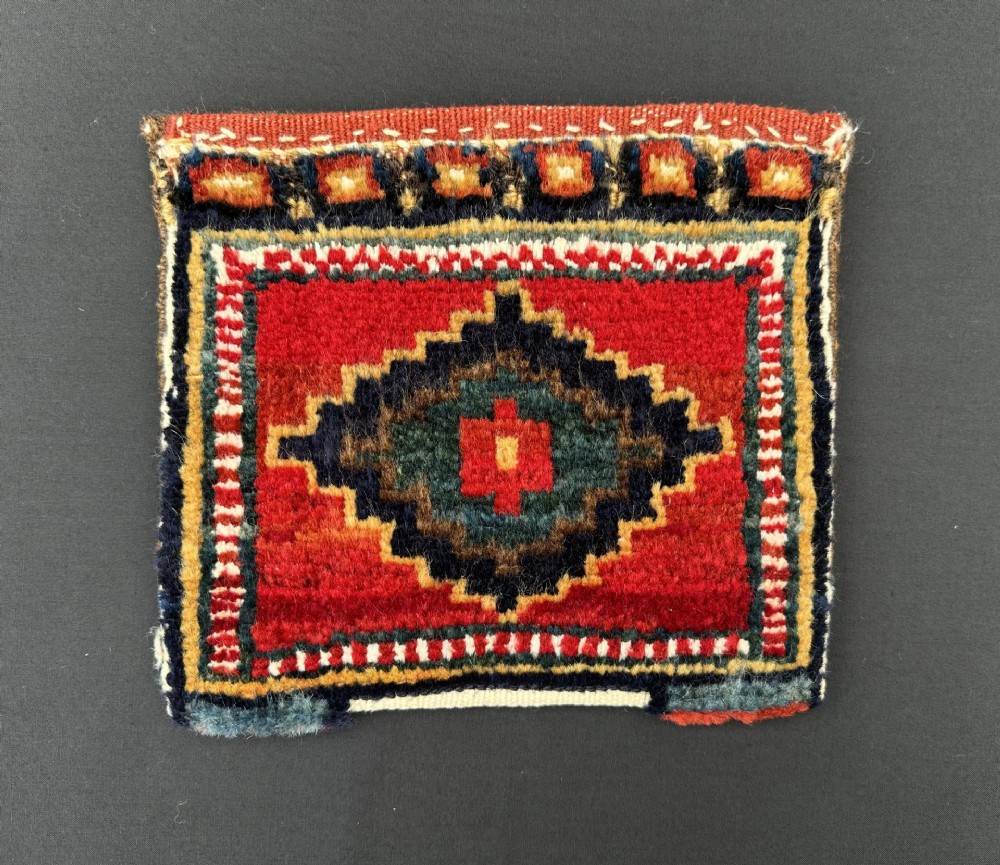 A small square hand-woven tribal bag featuring a central geometric diamond medallion in navy blue, red, and yellow surrounded by patterned borders.