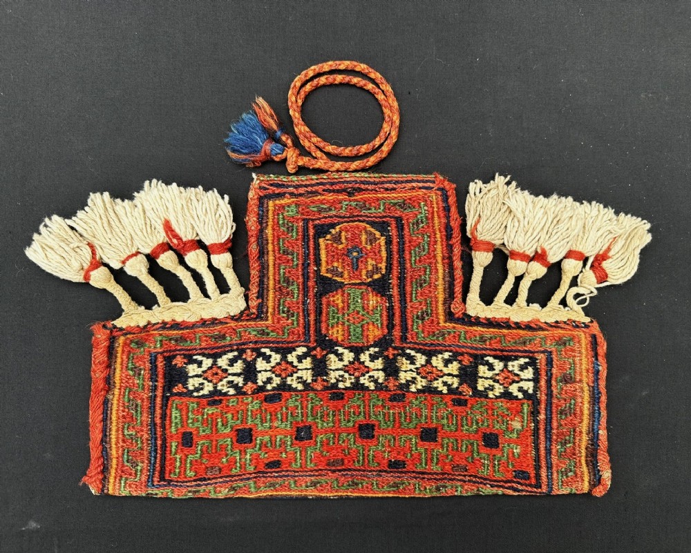 A small hand-woven Persian tribal wool pouch featuring geometric patterns in terracotta red, green, and navy with cream wool tassels.