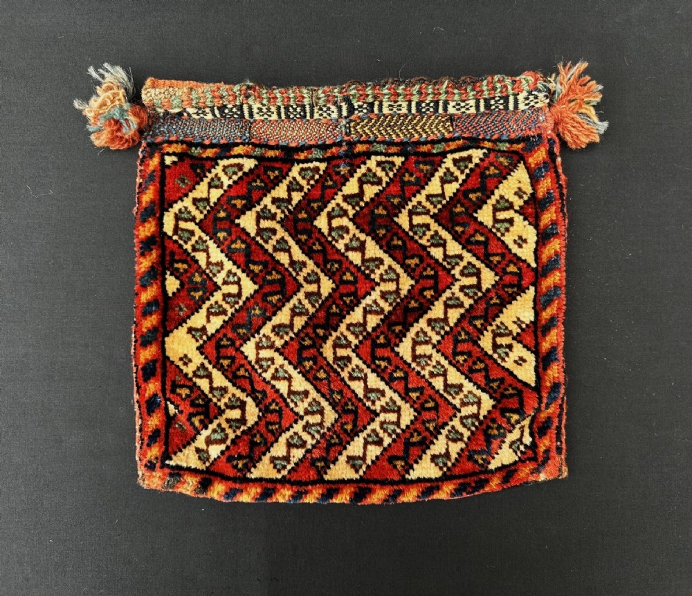 A square antique woven wool Qashqai vanity bag featuring red, navy, and ivory chevron patterns with braided edges and corner tassels.