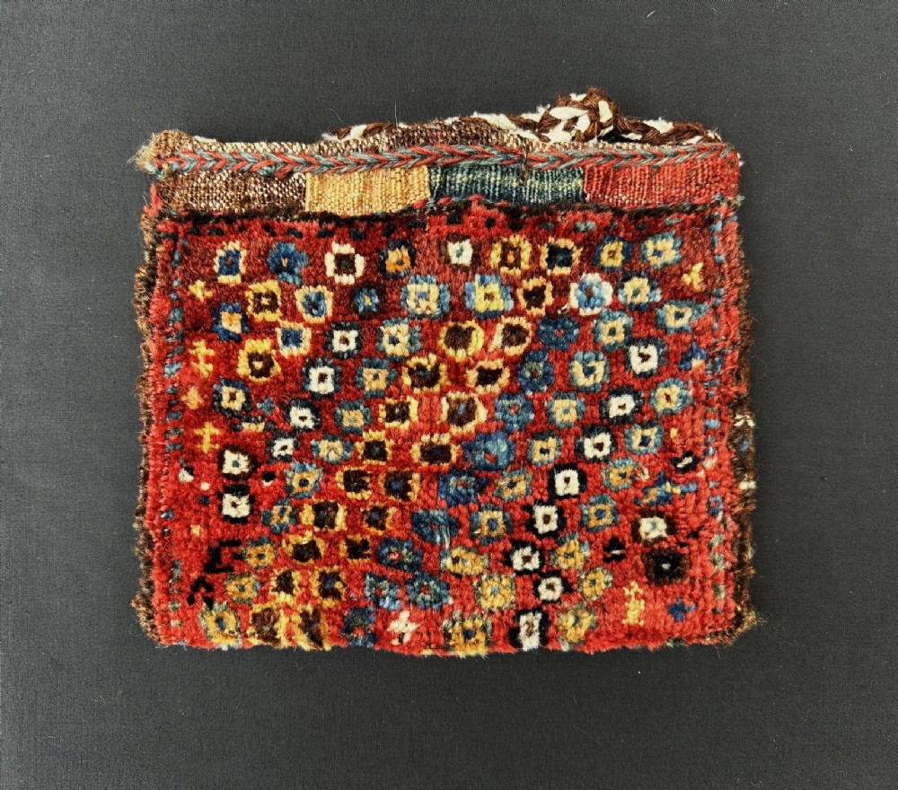 An antique handwoven Luri vanity bag with a dense geometric square pattern in red, blue, yellow, and white wool.