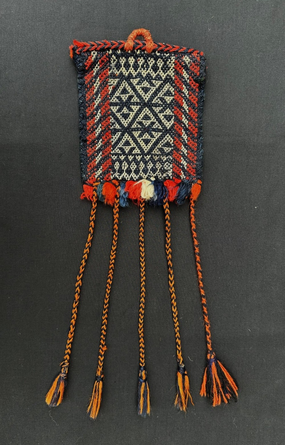 An antique flatwoven Qashqai tribal vanity bag featuring dark navy and ivory geometric diamond patterns with terracotta borders and lower braided tassels.