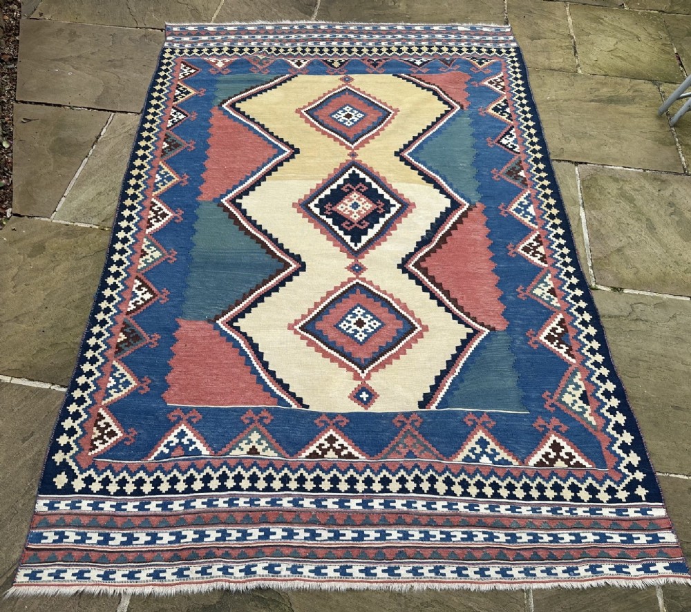 An antique Luri flatweave kilim featuring three interconnected cream diamond medallions set against a blue and terracotta geometric field.