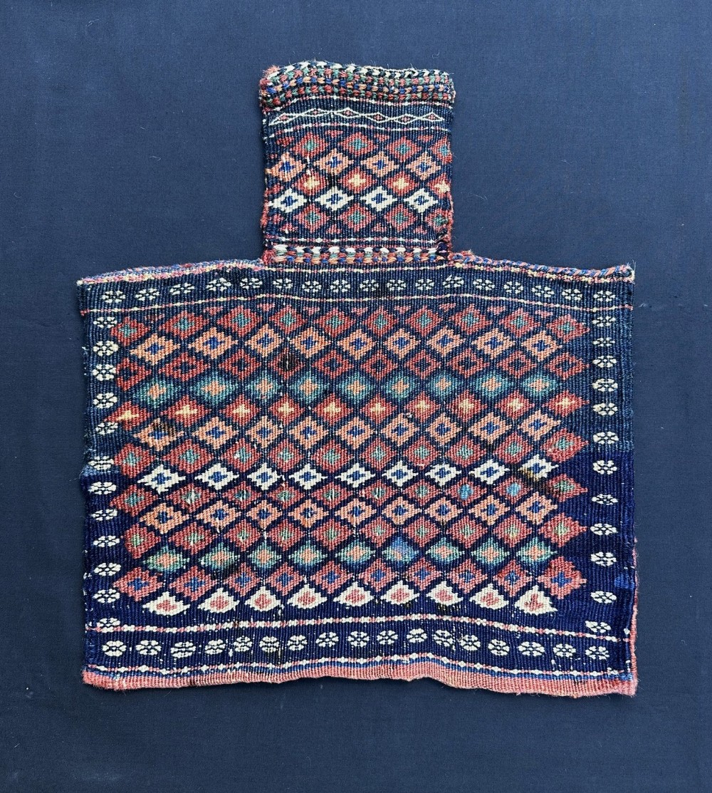 A handwoven antique wool salt bag featuring a narrow neck and geometric diamond lattice pattern in indigo blue, terracotta, and ivory.