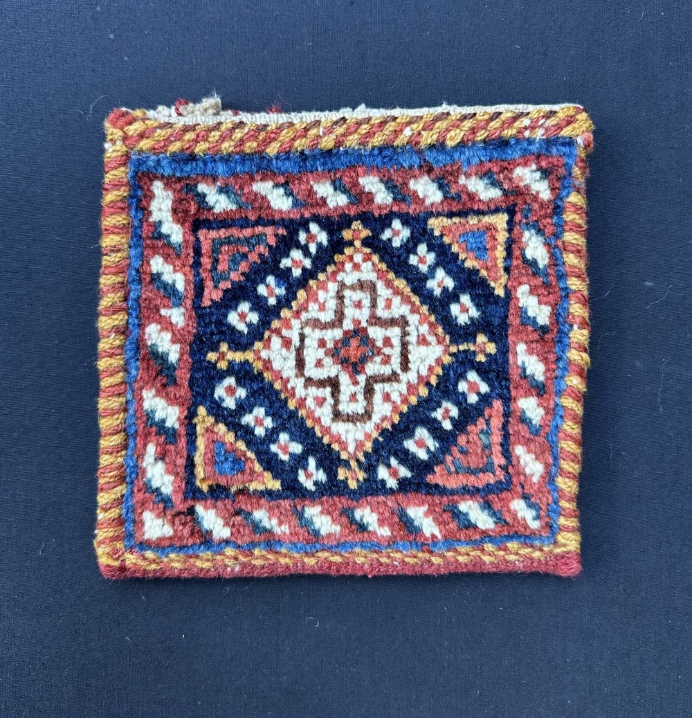 A square handwoven Persian Afshar wool vanity bag face featuring a central geometric diamond medallion in dark blue, terracotta red, and cream with wrapped overcast edges.