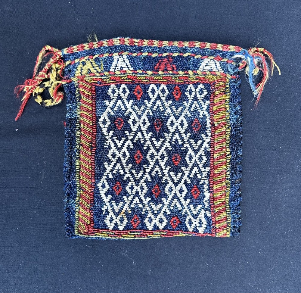 A small antique Persian tribal bag woven in indigo blue wool with geometric diamond patterns in ivory and red.