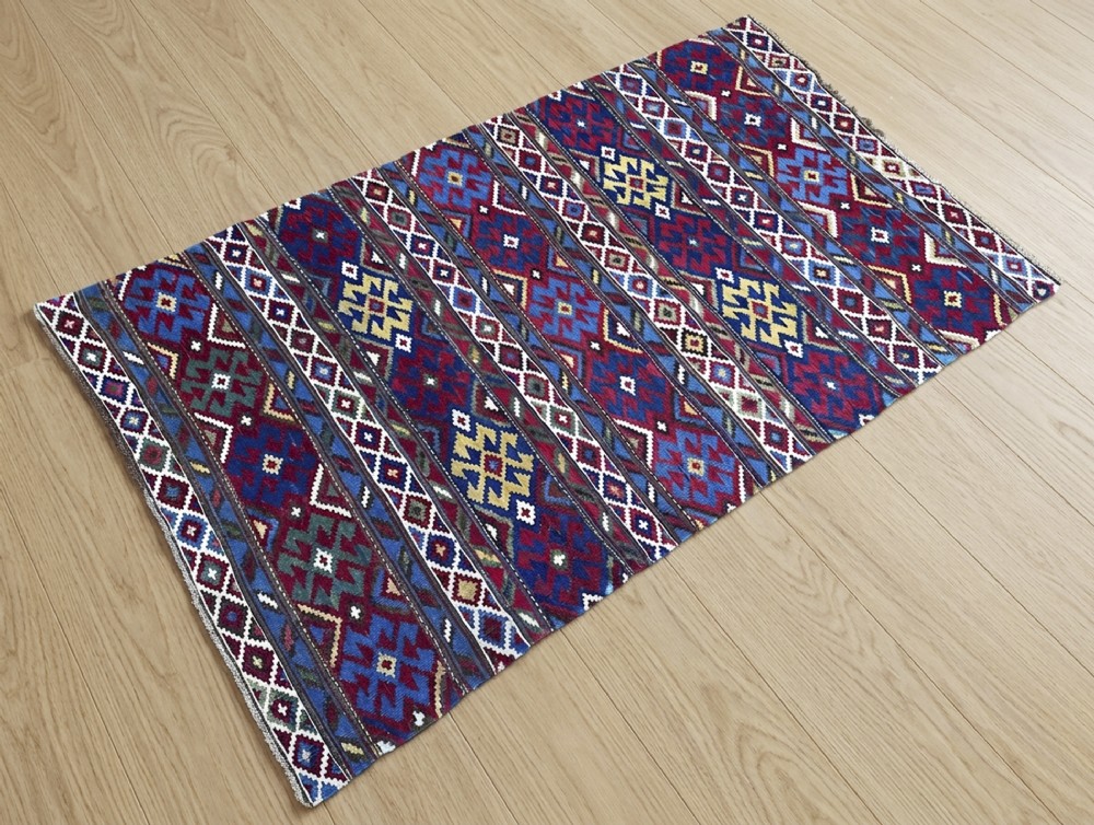 An antique flat-woven wool Shirvan kilim rug featuring horizontal bands filled with polychrome geometric patterns in shades of red, blue, yellow, green, and white.