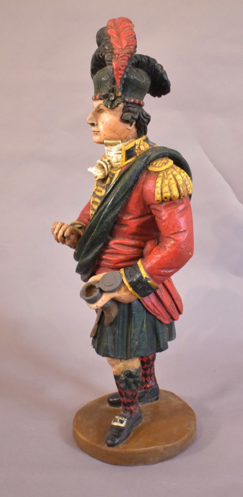 A carved and painted wooden figure of a Scottish Highlander soldier wearing a red jacket, kilt, and feathered bonnet. View VI