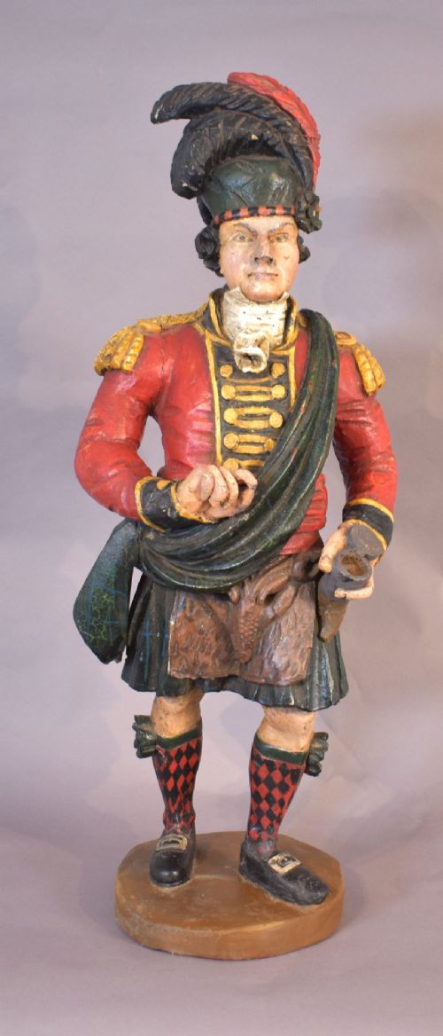 A carved and painted wooden figure of a Scottish Highlander soldier wearing a red jacket, kilt, and feathered bonnet. View VII