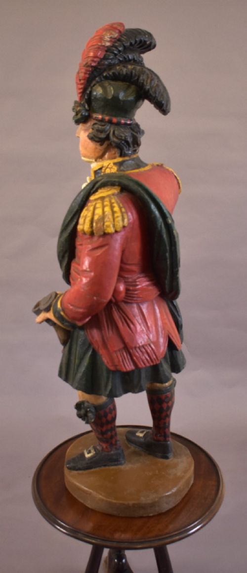 A carved and painted wooden figure of a Scottish Highlander soldier wearing a red jacket, kilt, and feathered bonnet. View VIII