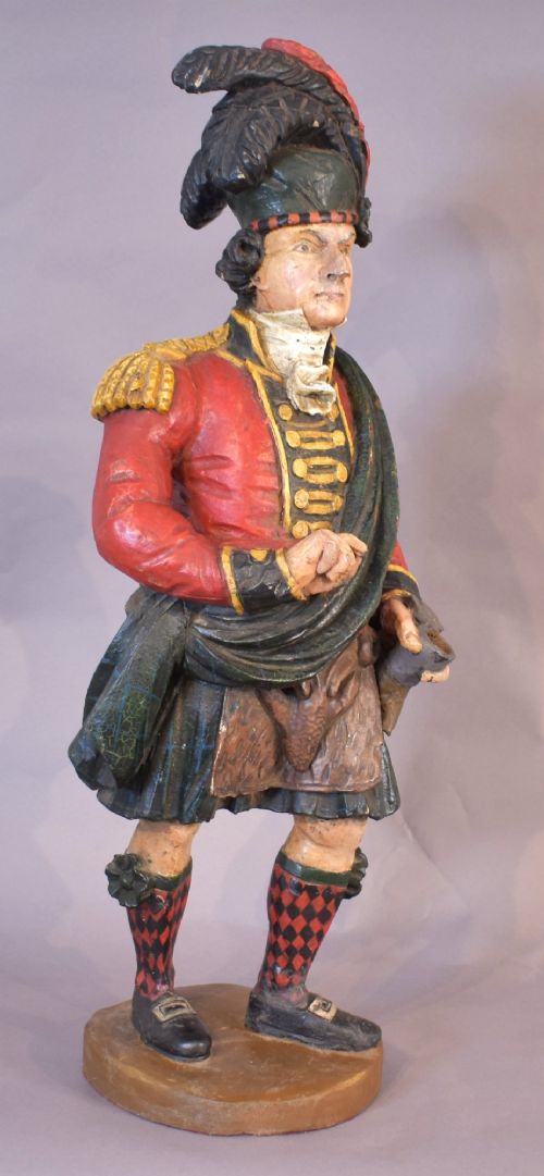 A carved and painted wooden figure of a Scottish Highlander soldier wearing a red jacket, kilt, and feathered bonnet. View IX