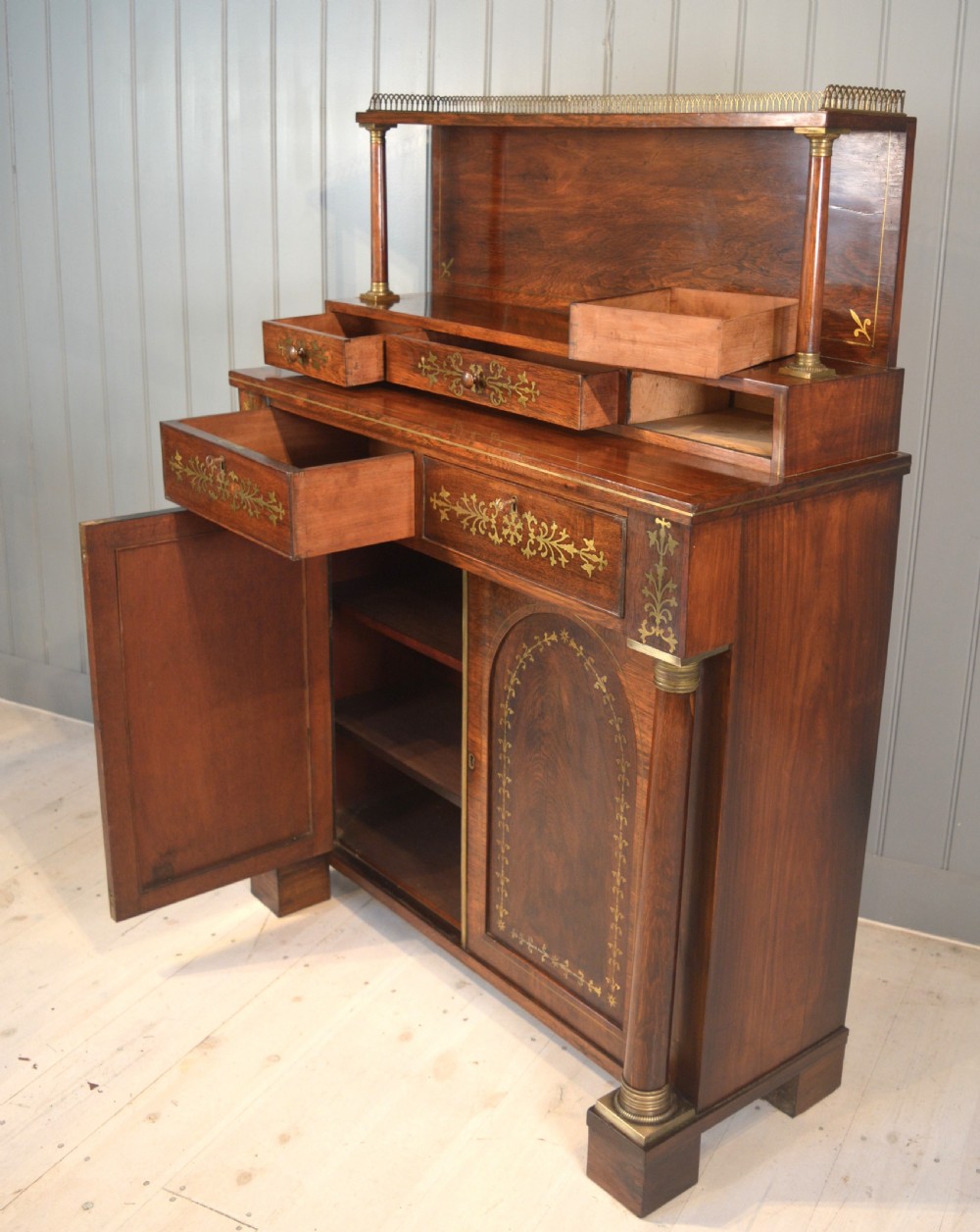 A dark rosewood Regency chiffonier side cabinet featuring brass foliate marquetry, a two-door arched cupboard, drawer storage, and a top shelf with a brass gallery. View III