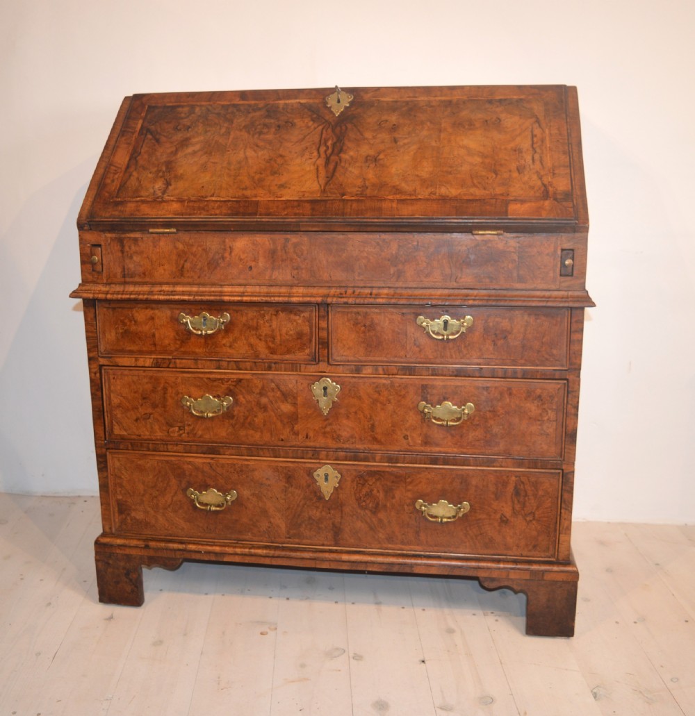 A burr walnut slant-front bureau featuring brass drop handles, keyhole escutcheons, and a lower chest of drawers set on bracket feet.