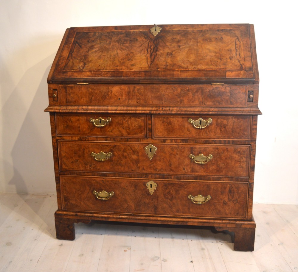 A burr walnut slant-front bureau featuring brass drop handles, keyhole escutcheons, and a lower chest of drawers set on bracket feet. View II