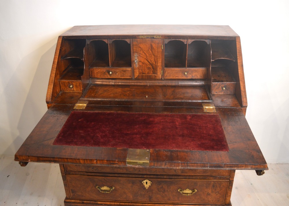 A burr walnut slant-front bureau featuring brass drop handles, keyhole escutcheons, and a lower chest of drawers set on bracket feet. View III
