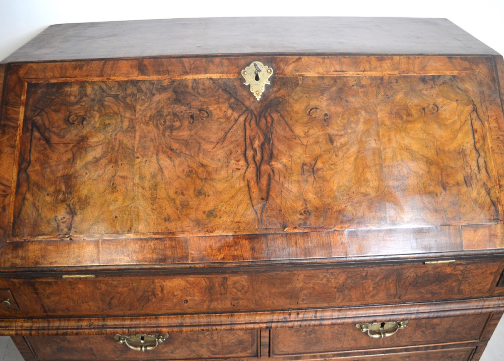 A burr walnut slant-front bureau featuring brass drop handles, keyhole escutcheons, and a lower chest of drawers set on bracket feet. View V