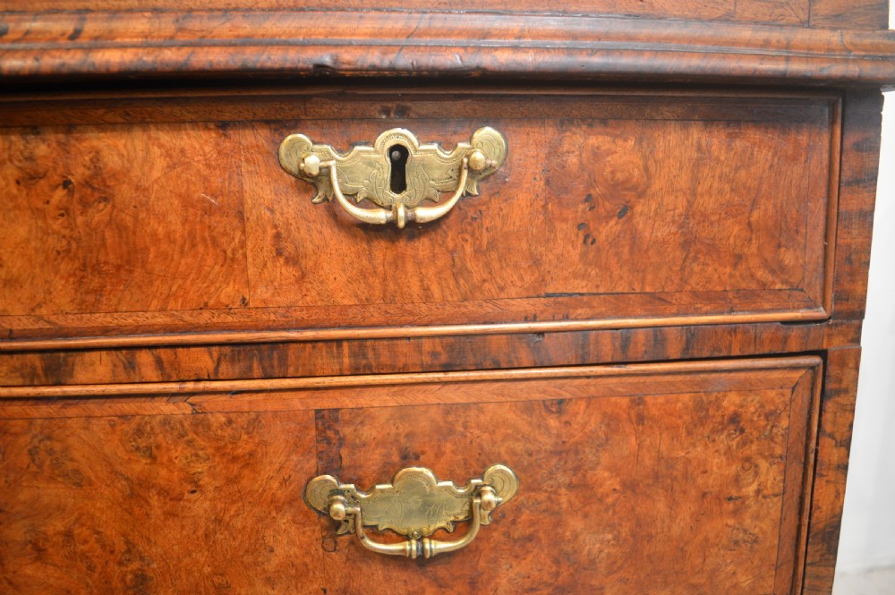 A burr walnut slant-front bureau featuring brass drop handles, keyhole escutcheons, and a lower chest of drawers set on bracket feet. View VI