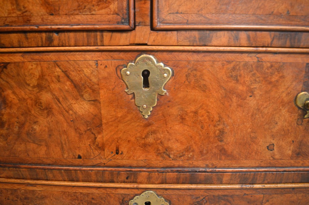 A burr walnut slant-front bureau featuring brass drop handles, keyhole escutcheons, and a lower chest of drawers set on bracket feet. View VII