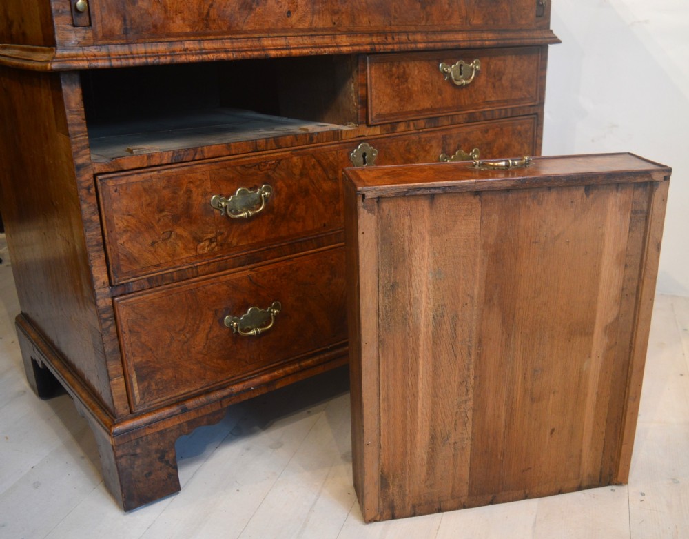 A burr walnut slant-front bureau featuring brass drop handles, keyhole escutcheons, and a lower chest of drawers set on bracket feet. View IX