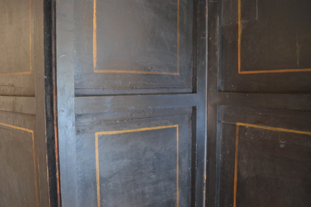 A four-panel antique folding room screen featuring painted classical architectural columns, figures in period dress, and scrolling acanthus base motifs with studded brass edging. View X