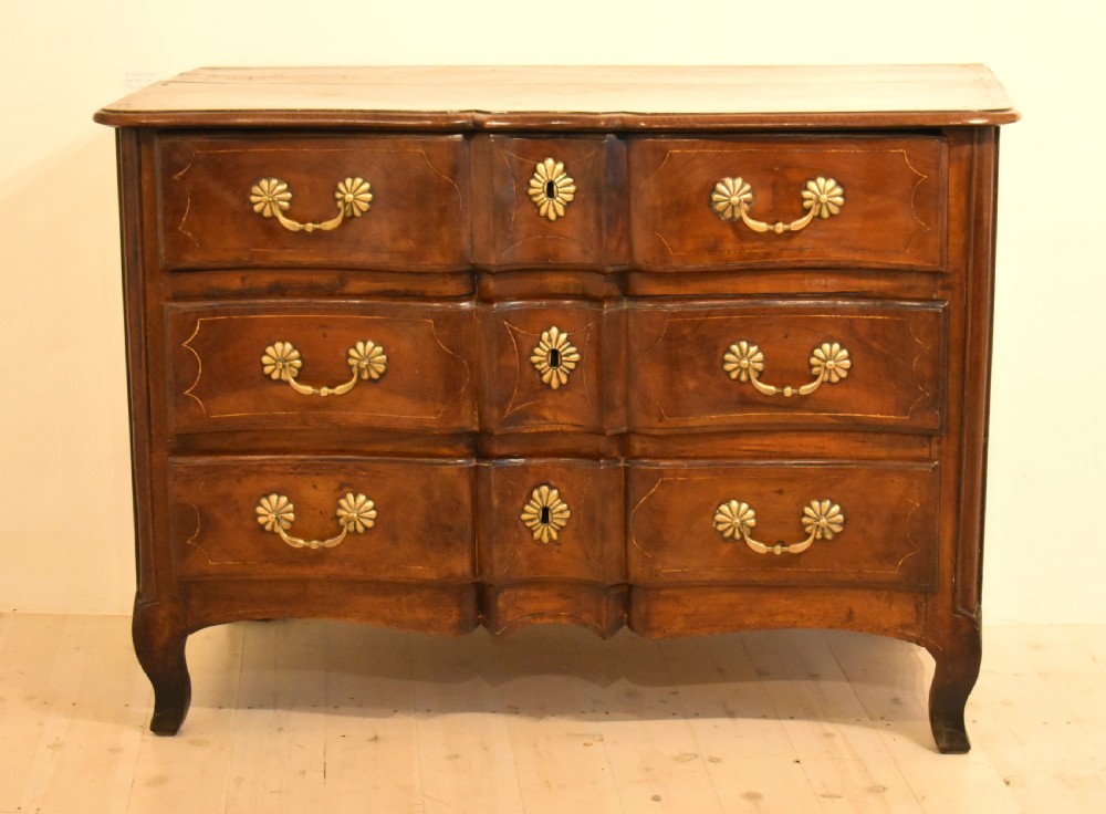 A French provincial walnut commode with three long drawers featuring brass rosette drop handles, keyhole escutcheons, and curved legs.