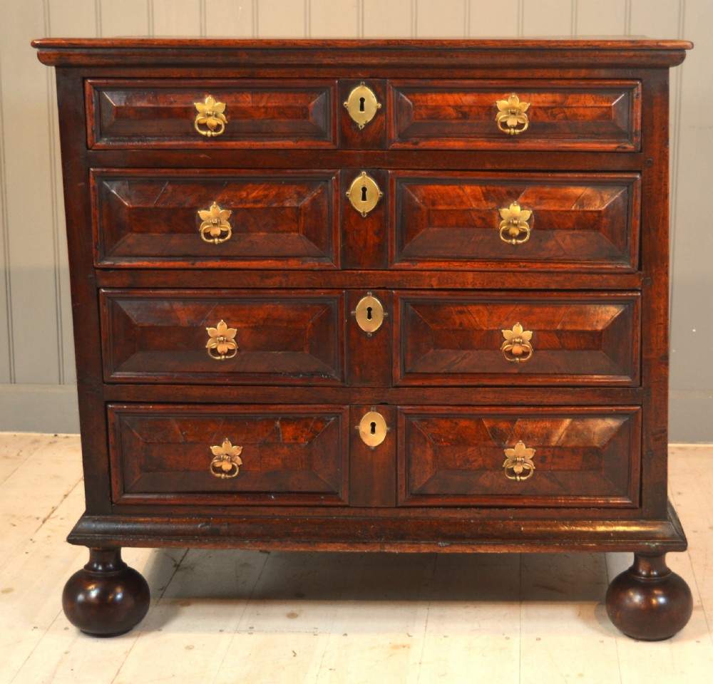 A 17th-century walnut chest of drawers with four moulded drawer fronts, brass drop handles, brass keyhole escutcheons, and large turned bun feet. View II
